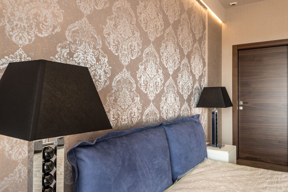 Bedroom with soft damask wallpaper and a blue velvet upholstered headboard