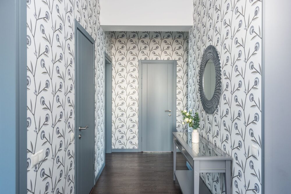 Bright entry hallway with delicate white floral wallpaper, a console table and round mirror