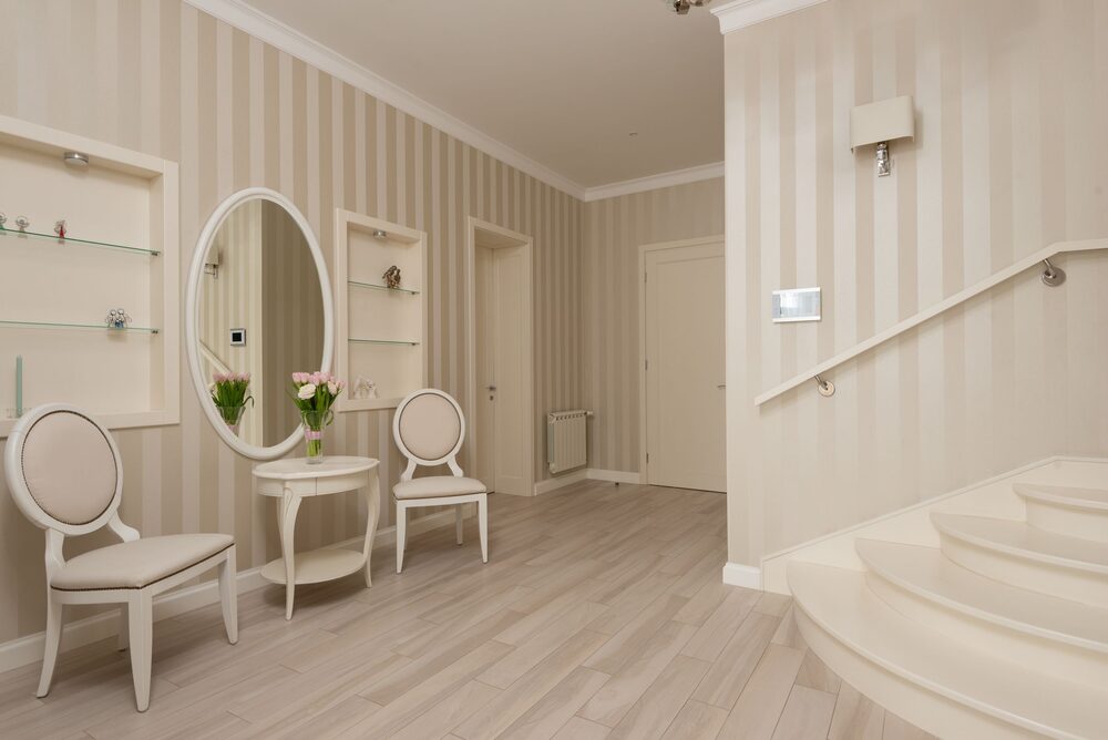 Classic hallway with soft striped beige wallpaper and an oval mirror