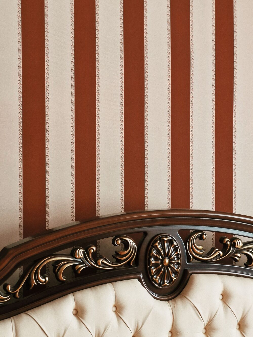 Bedroom with warm rust and cream striped wallpaper behind a tufted headboard