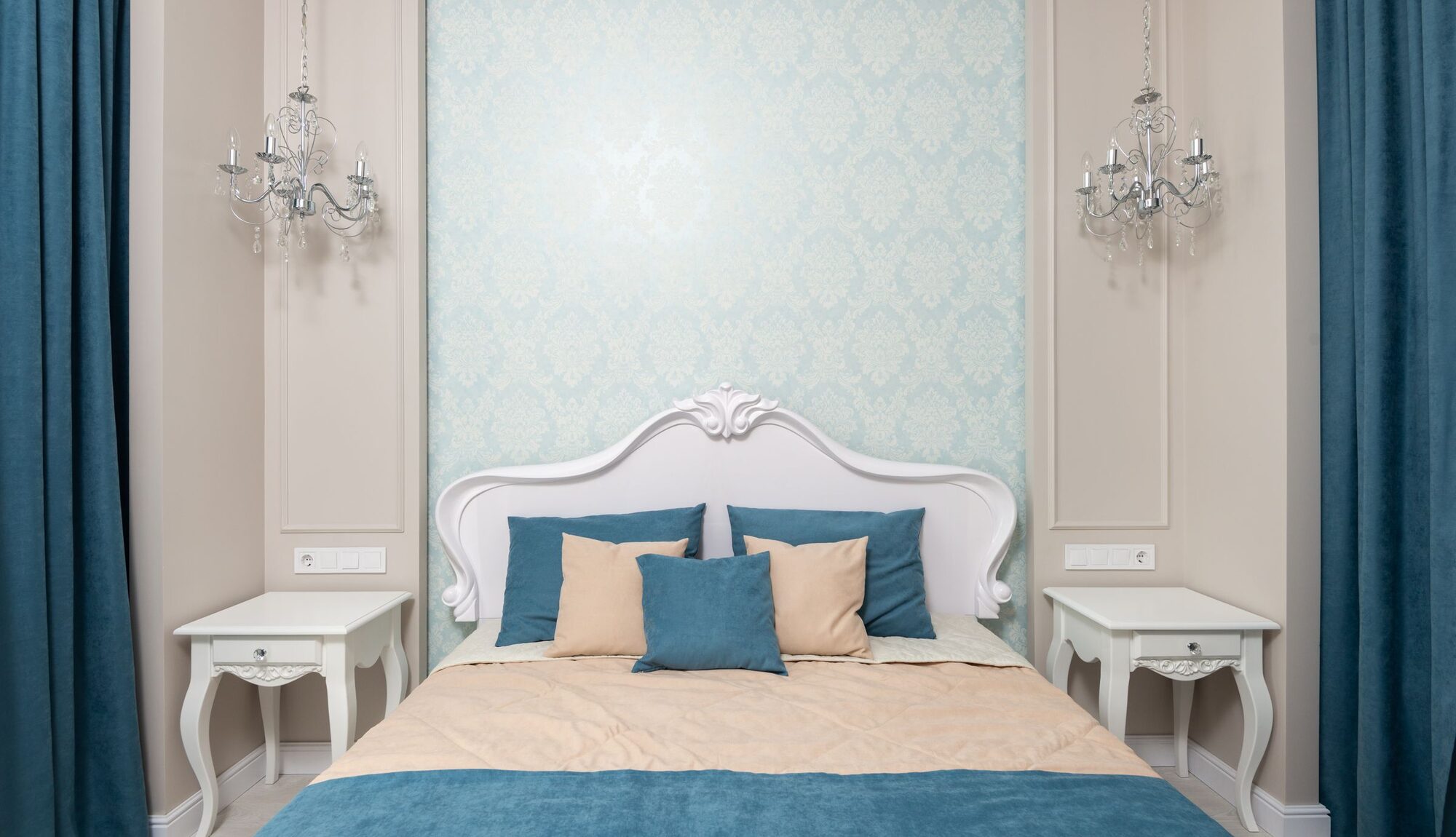 Elegant residential bedroom with softly patterned damask wallpaper, chandeliers and a tailored upholstered bed